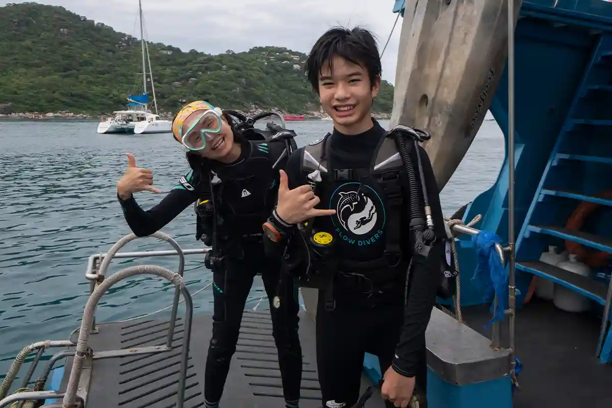 Continue to the PADI Open Water Course in Koh Tao Two divers in scuba equipment smiling on a dive boat in Koh Tao