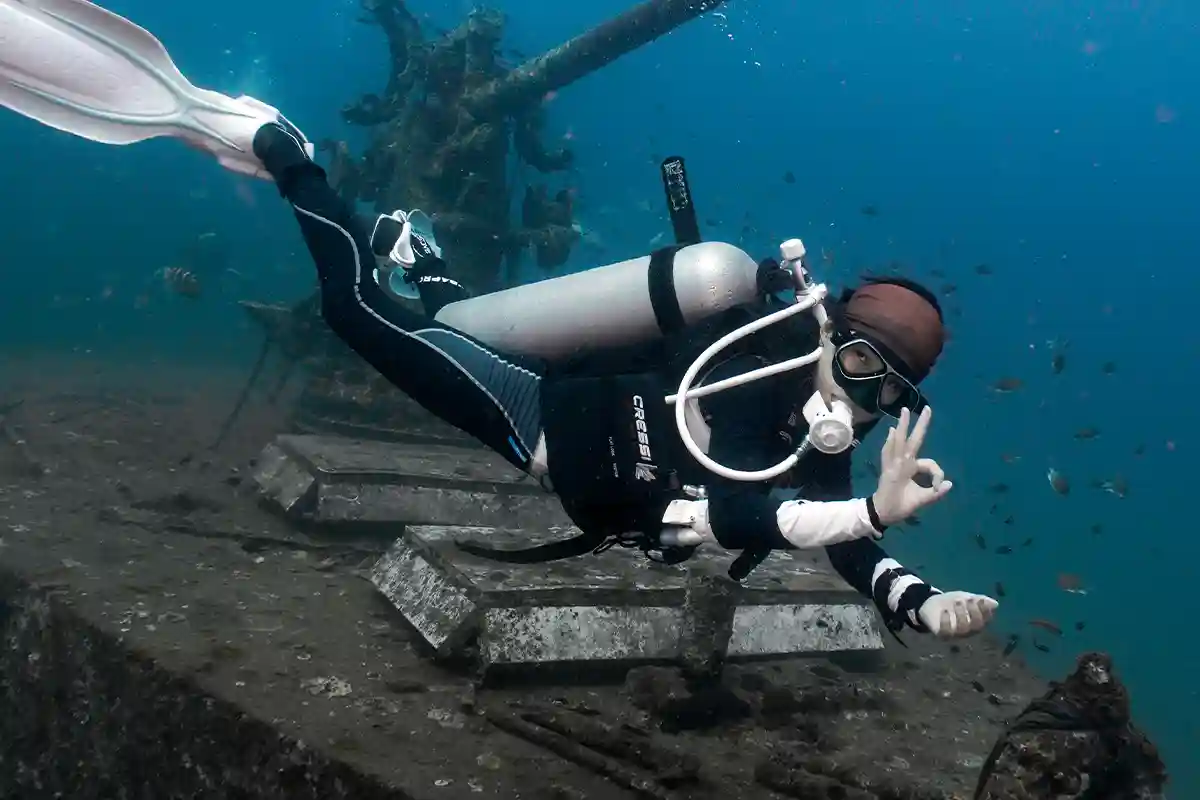 Diver Beside the Deck Gun in Koh Tao Scuba diver giving an OK sign beside the deck gun on a shipwreck in Koh Tao