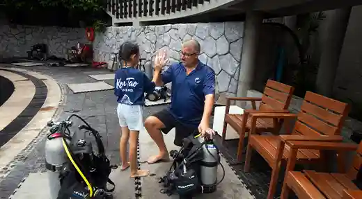 PADI Bubblemaker Briefing in Koh Tao Child and PADI Professional during a Bubblemaker briefing beside scuba equipment in Koh Tao.