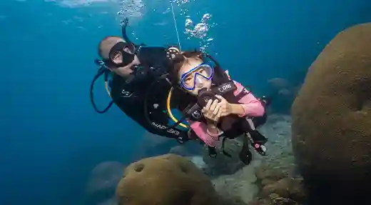 PADI Bubblemaker Ocean Dive in Koh Tao Child scuba diving with a PADI Professional beside coral during a Bubblemaker Experience in Koh Tao.