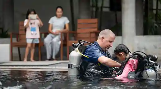 PADI Bubblemaker Pool Preparation in Koh Tao PADI Professional helping a child with scuba equipment before a Bubblemaker pool session in Koh Tao.