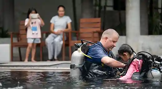 PADI Bubblemaker Pool Training in Koh Tao PADI Professional helping a child with scuba equipment during a Bubblemaker pool session.
